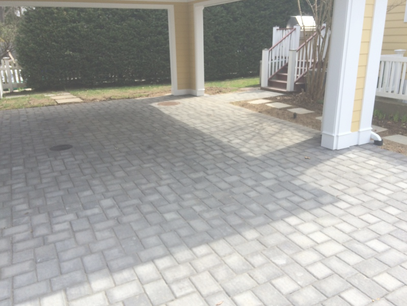 Brick driveway leading to a covered entrance with steps, yellow columns, and white fence.