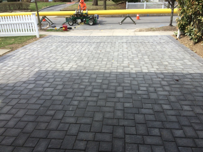 Driveway with patterned gray pavers; road work with orange cones and yellow pipe in background.