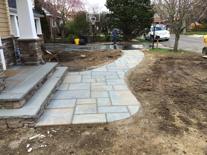 Stone walkway and steps leading to a house entrance. Construction in progress, dirt and equipment visible.