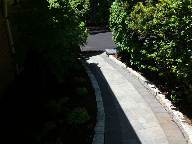 Stone pathway bordered by bushes and a dark mulched garden.