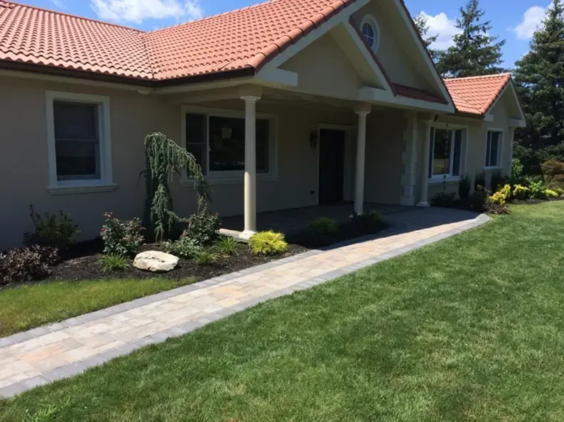 Beige house with terracotta roof, paved walkway, green lawn, and landscaped garden.