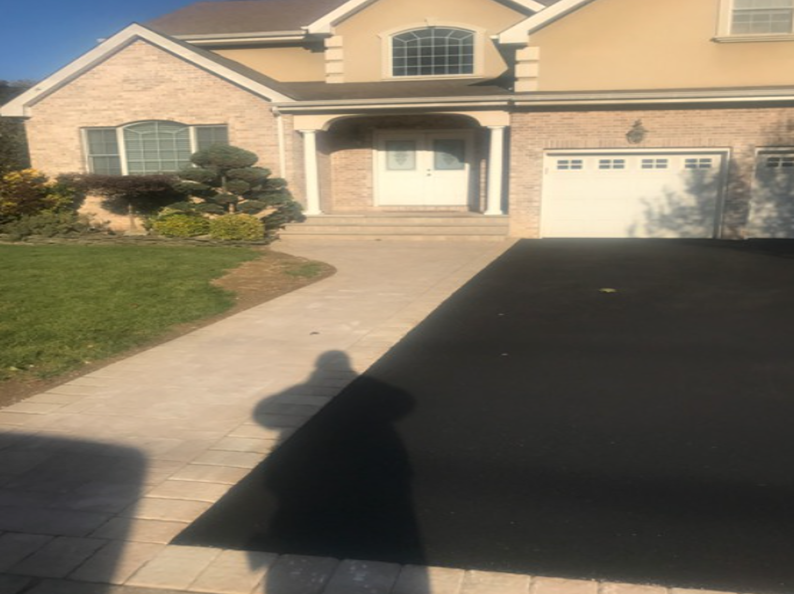Tan brick and stucco house with a black asphalt driveway, concrete walkway and manicured lawn.