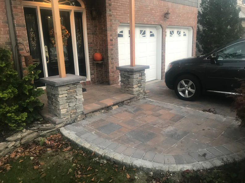 Stone pillars frame a brick entryway with a black car parked nearby.