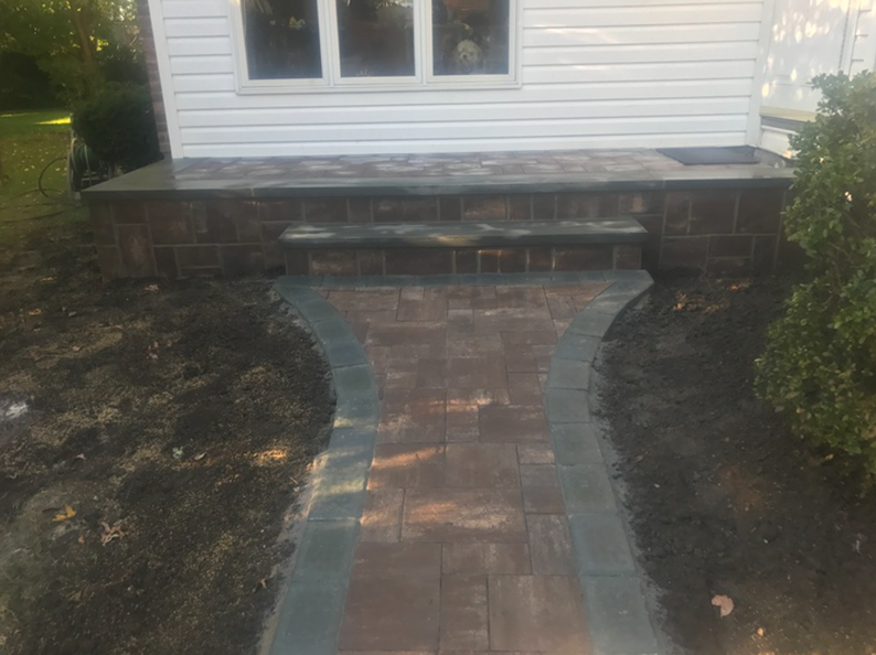 Brick walkway leading to steps and a house with white siding and a window.