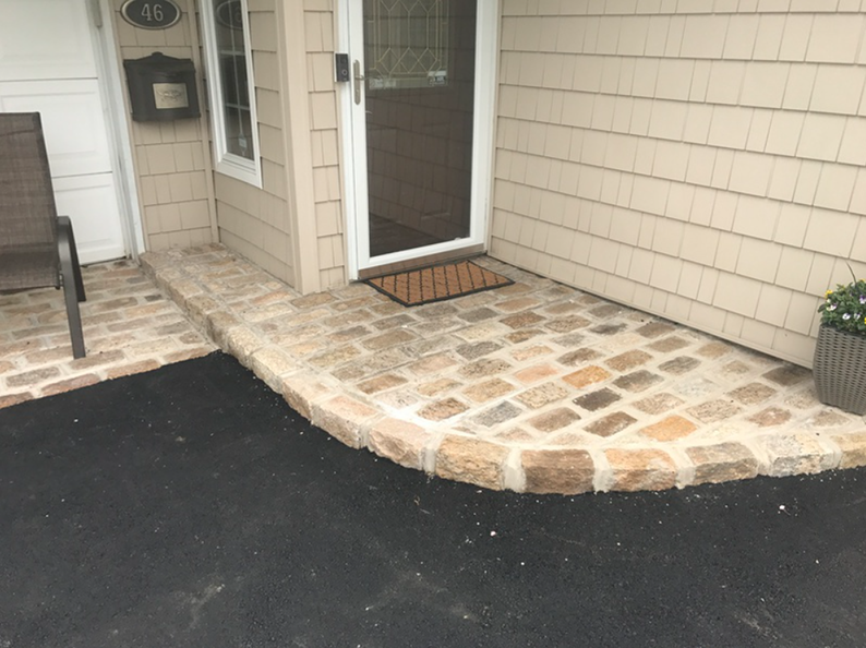 Brick walkway and landing with a curved edge, leading to a front door, asphalt driveway.