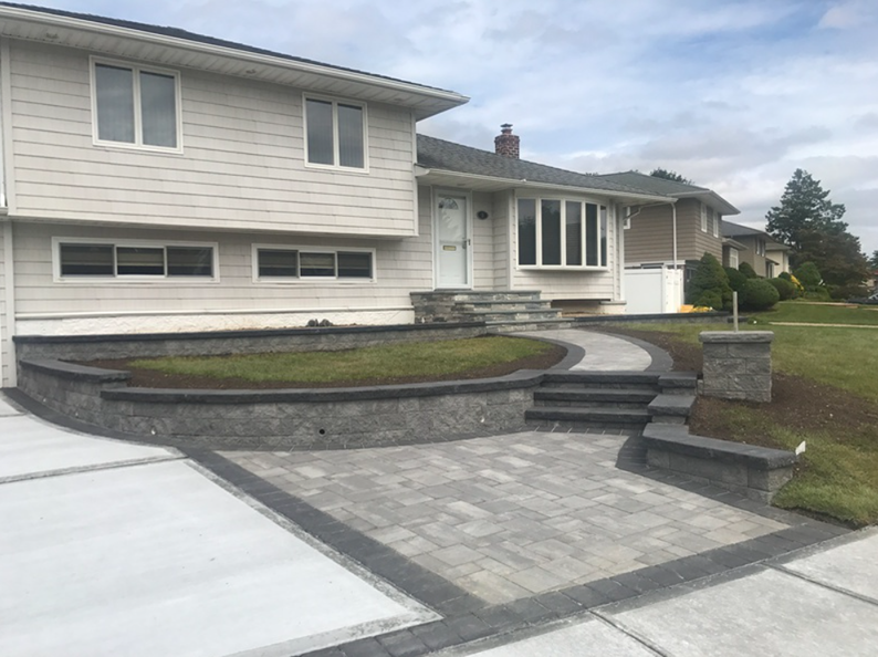 A house with a renovated front yard featuring a gray brick patio, retaining walls, and steps.