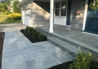 Stone walkway leading to a house with a blue door, steps, and a white column.