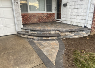 Brick and stone front porch with steps; driveway and garage to the left, grass to the right.