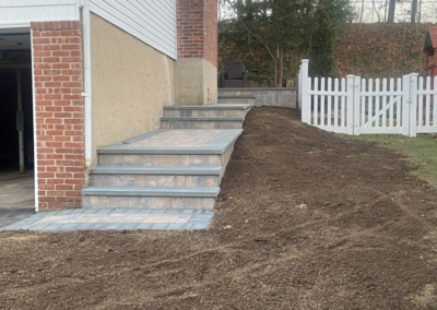Brick steps leading up a hill, next to a garage and white picket fence. Newly laid topsoil.