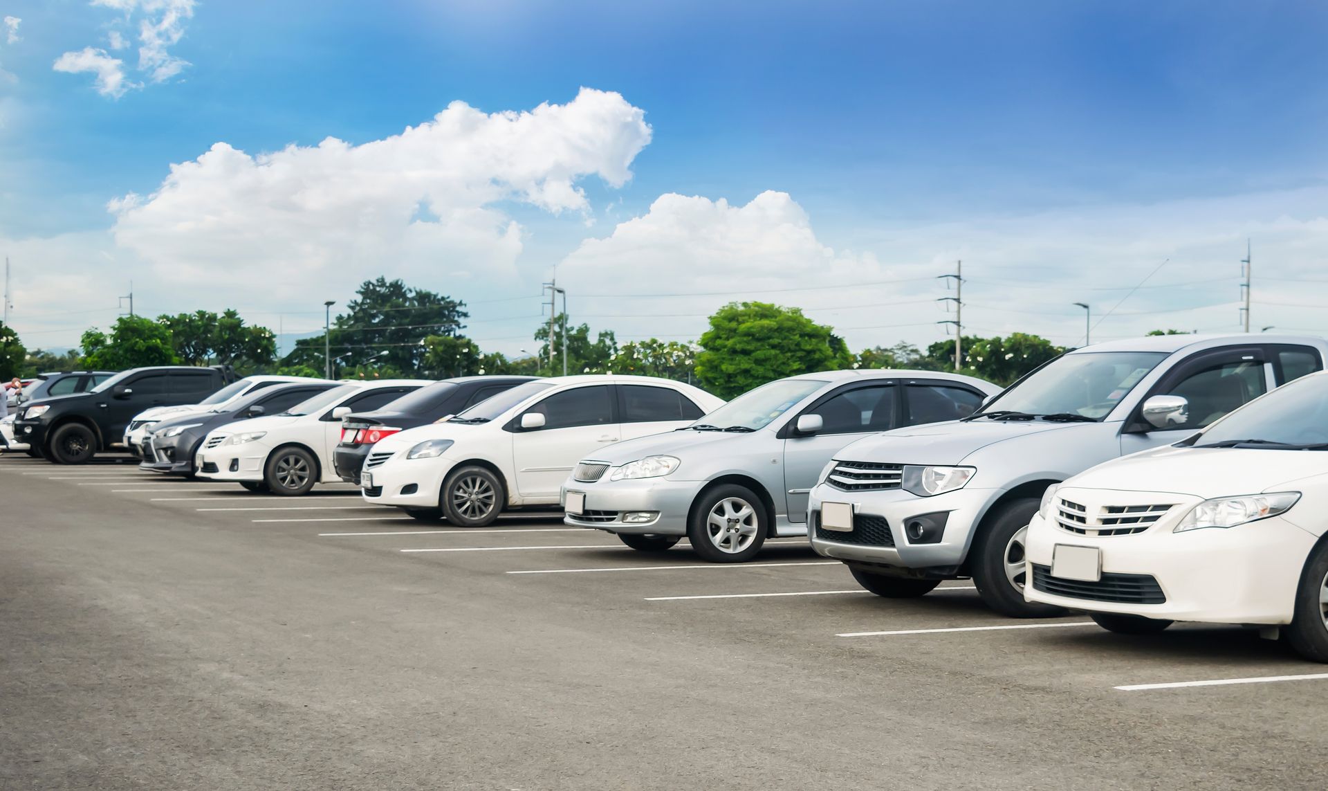 A row of white cars are parked in a parking lot.