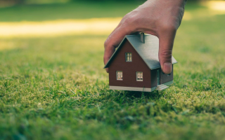 A person is holding a small model house in the grass.