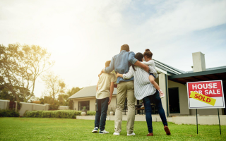 A family is standing in front of a house for sale.