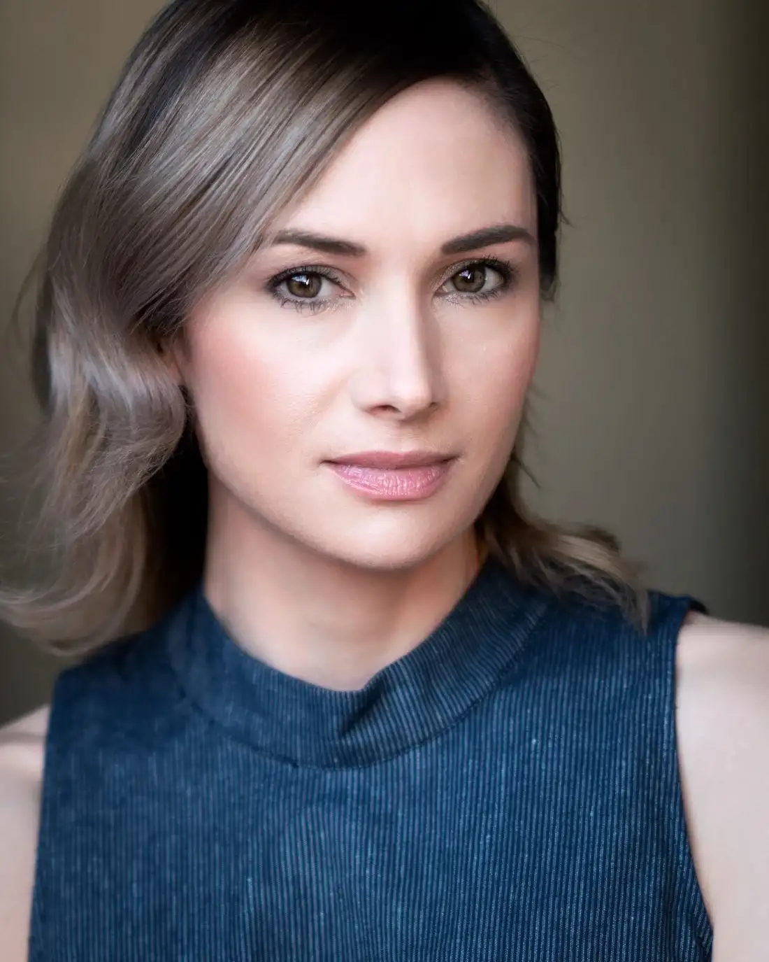 A woman is wearing a blue tank top and looking at the camera.