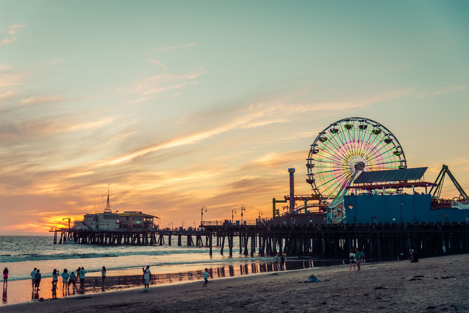 There is a ferris wheel on the pier at sunset.