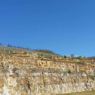 Cliff face with layers of tan rock against a bright blue sky.