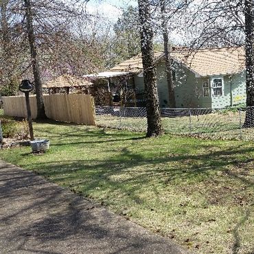 A green house with a wooden fence and a small front yard, surrounded by trees.