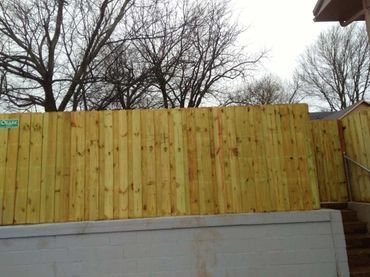 Wooden fence on a concrete foundation, with bare trees in the background.