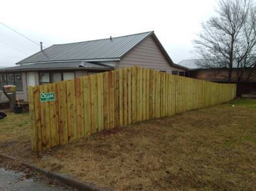 Wooden fence curving along a yard beside a beige house under a gray sky.