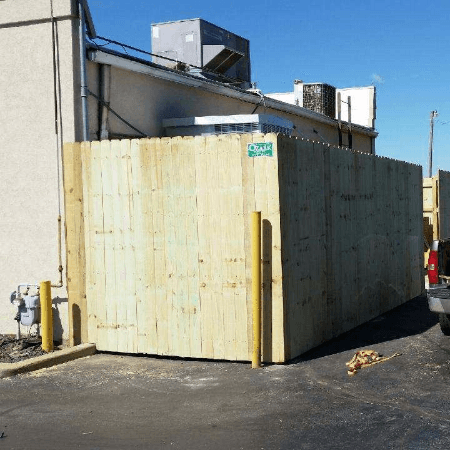 Wooden fence enclosing a building's exterior, with yellow bollards nearby.