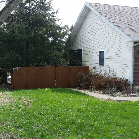 Brown fence beside a beige house with a small window and overgrown grass.