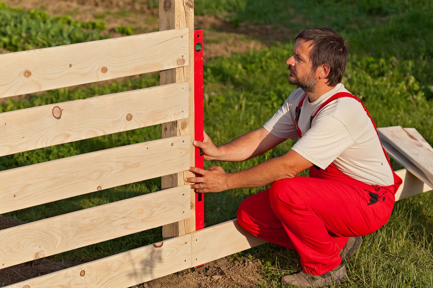 A worker installing a wooden privacy fence in a commercial property.