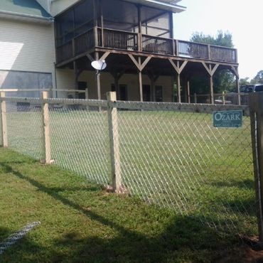 Chain link fence in front of a house with a wooden deck on a sunny day.