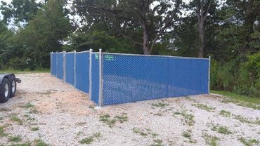Blue privacy fence in a gravel lot, trees in the background.