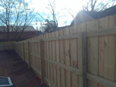 Wooden fence in a yard, sunny day with a blue sky and bare trees.