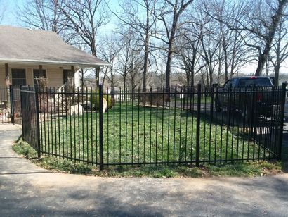 Black metal fence surrounds a green grassy yard next to a house and driveway.