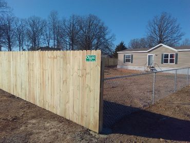 Wooden fence surrounding a house with chain-link gate; clear sky.