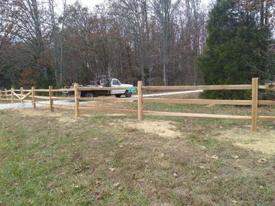 Wooden split-rail fence in front of a field, with a truck parked behind it.