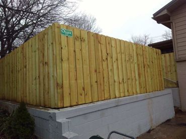Wooden fence on a concrete base, beside a house. Yellowish wood, overcast sky.