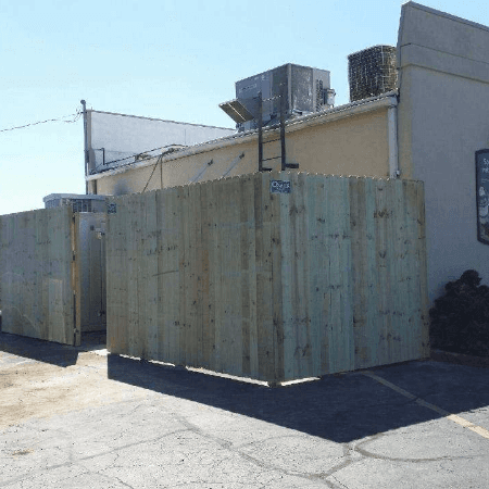 Wooden fence surrounds a building's mechanical equipment in an outdoor parking lot on a sunny day.