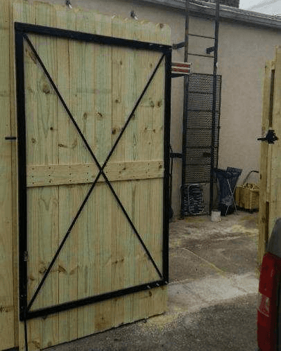 Wooden gate with black metal frame and diagonal cross supports, open in a paved area.