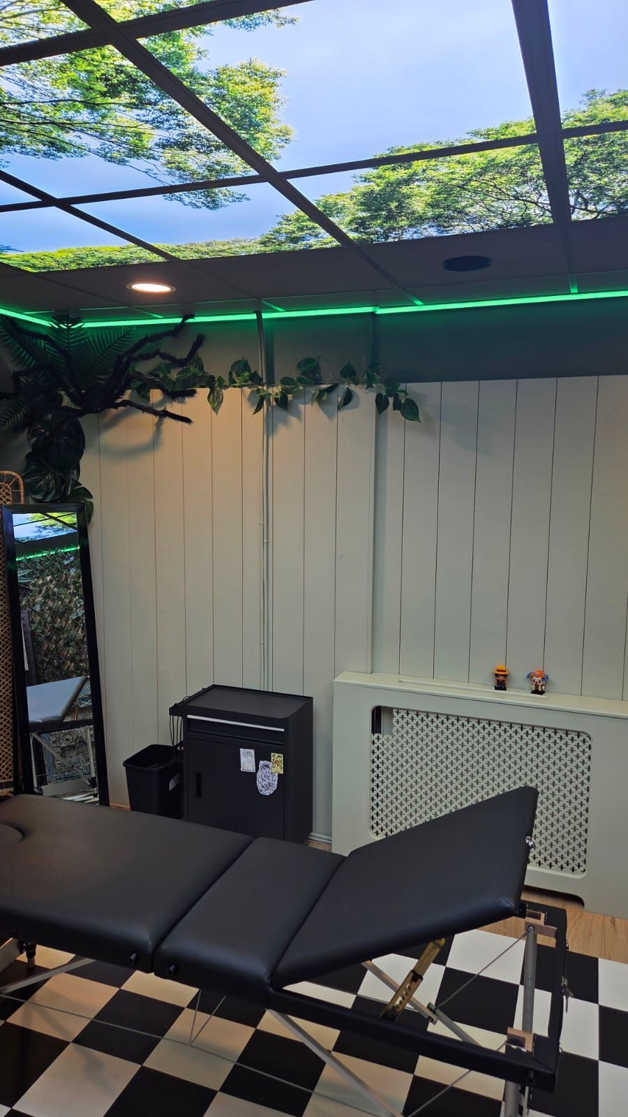Tattoo studio interior with a black table, checkered floor, white wall, and a ceiling with a nature scene.