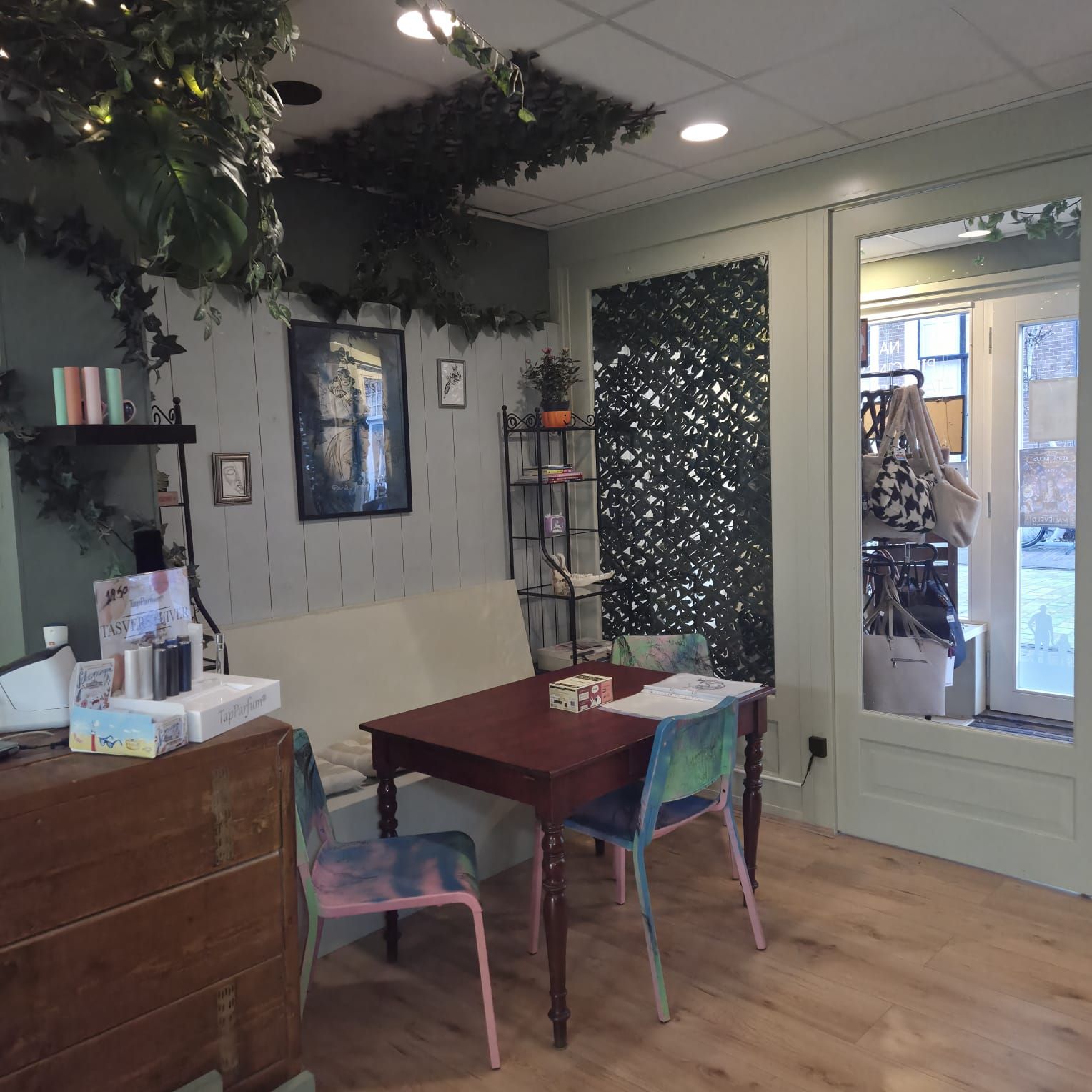 Interior with a table, chairs, sofa, and decorative greenery. Light wood floors, green walls, and a door to the outside.