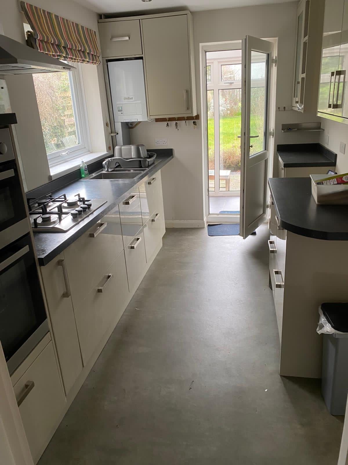 Narrow cream kitchen with dark countertops, gas stove, and open door to a garden.