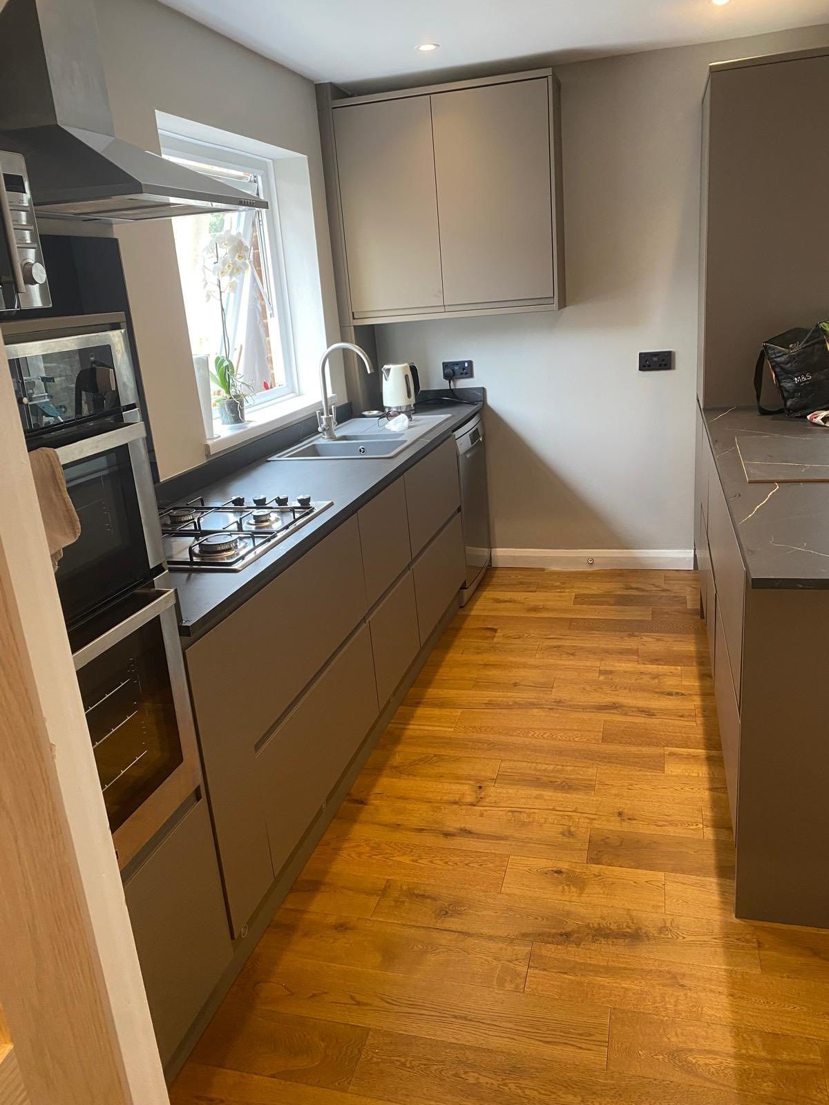 A modern kitchen with gray cabinets, dark countertops, wooden floors, and stainless steel appliances.