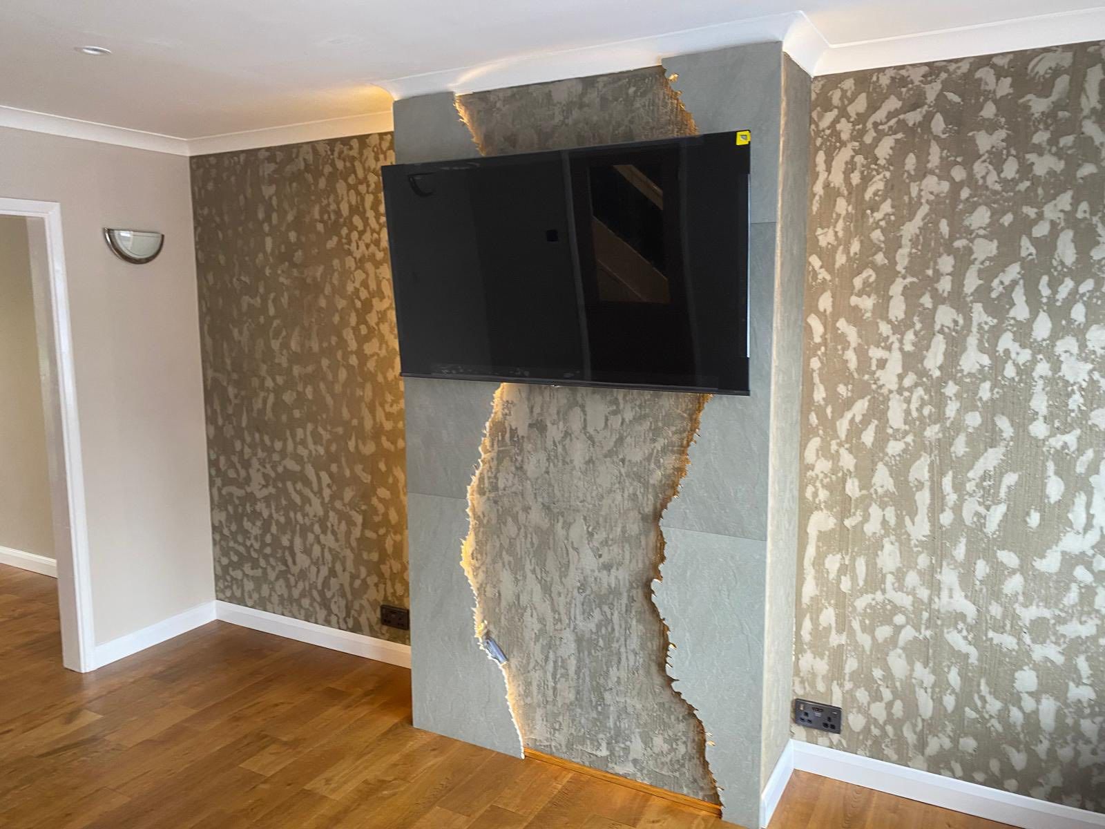 TV mounted on a stone accent wall with integrated lighting, flanked by patterned wallpaper and hardwood flooring.