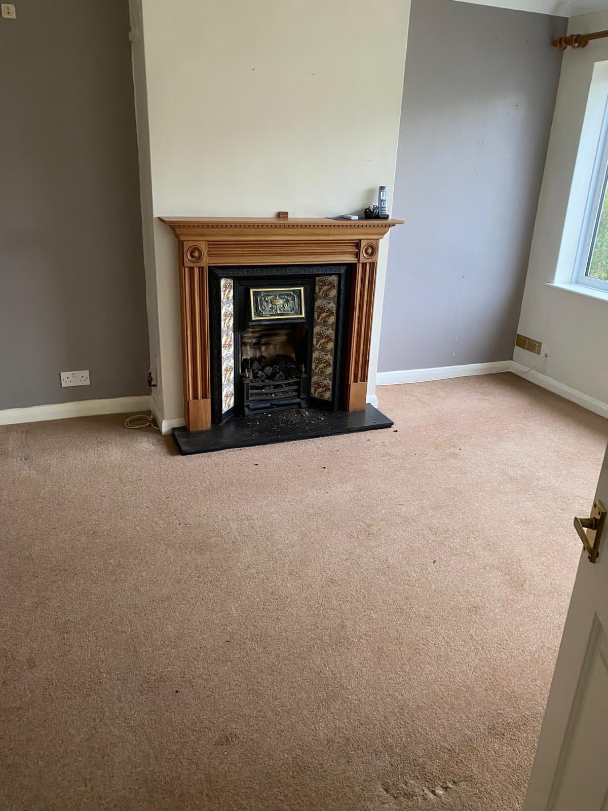 Empty room with fireplace, beige carpet, and two-tone walls (gray and off-white).