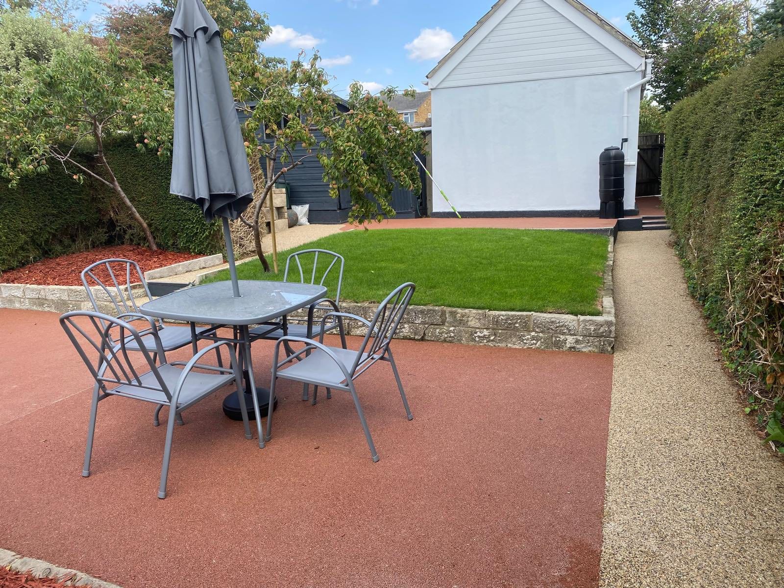 Outdoor patio with table and chairs, lawn, and garden; a gray umbrella is closed.