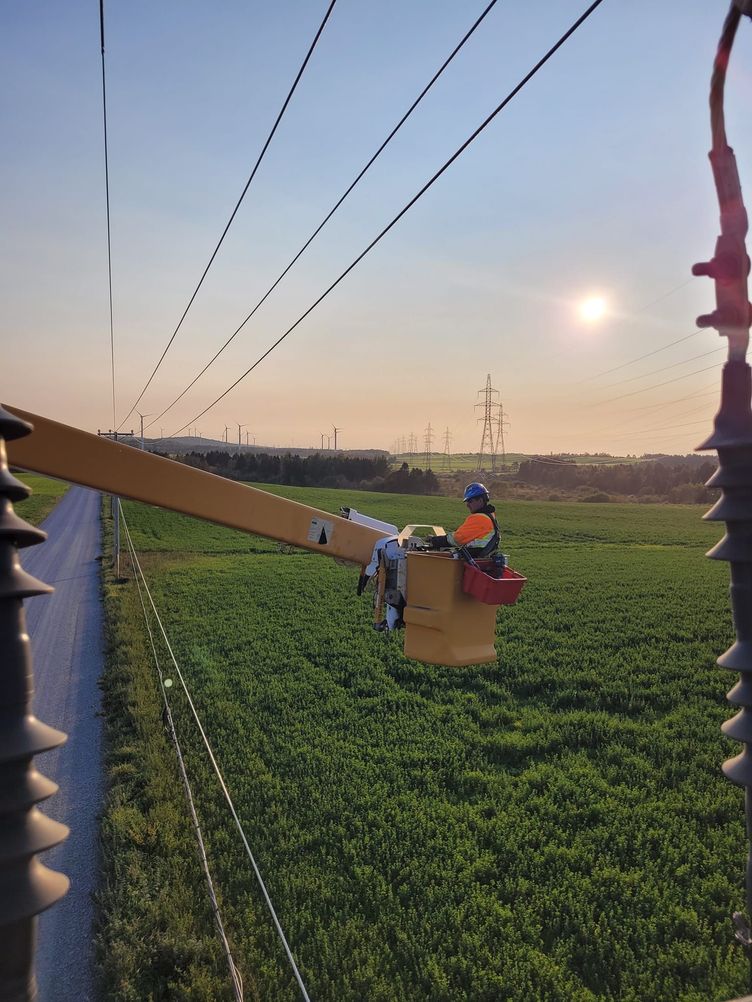 Un homme dans un seau travaille sur une ligne électrique dans un champ.