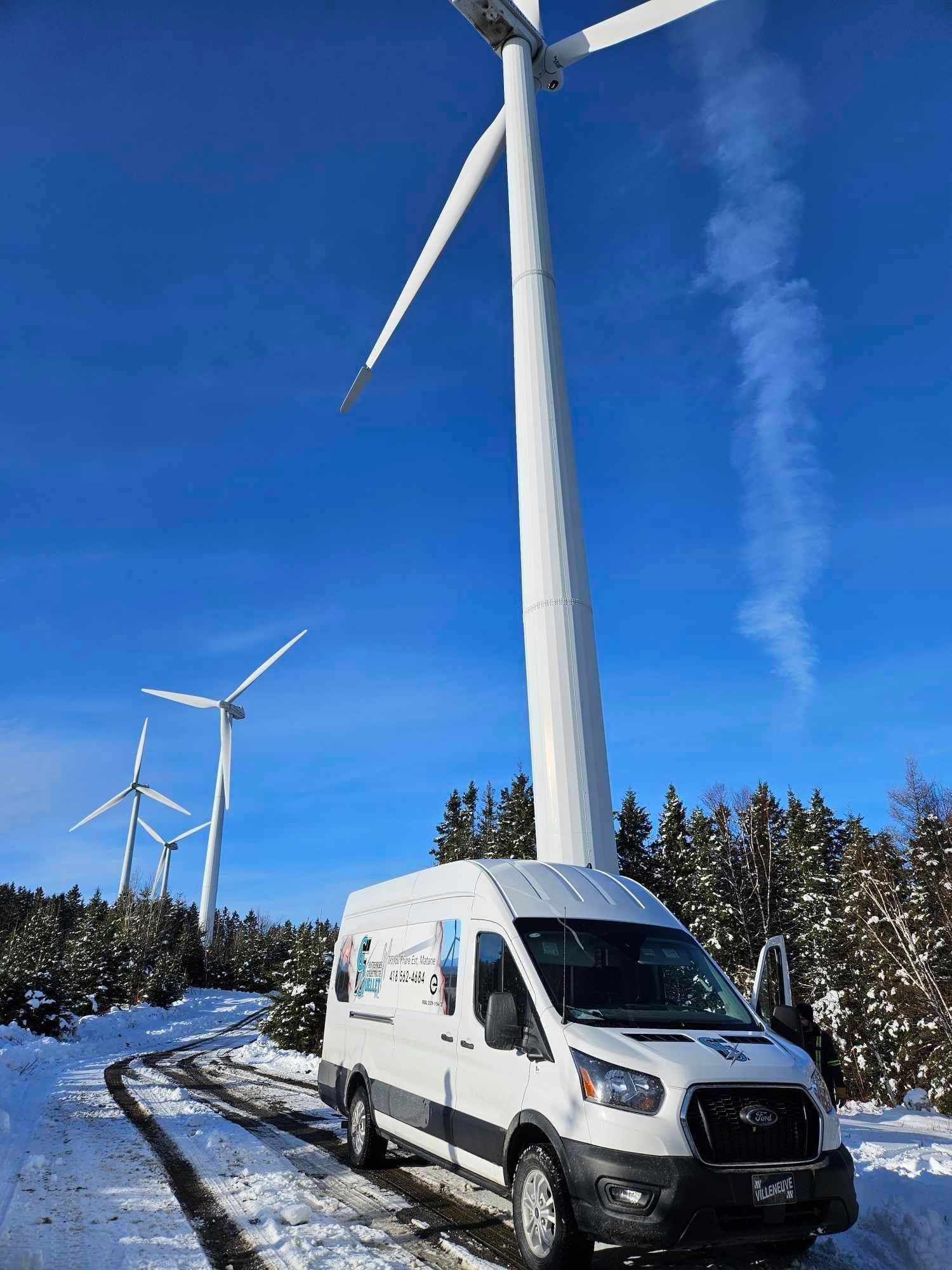 Une camionnette blanche est garée dans la neige devant un moulin à vent.