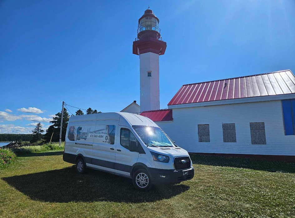 Une camionnette blanche est garée devant un phare.