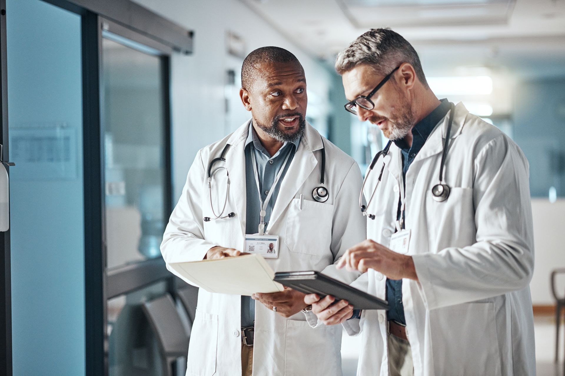 Two doctors are looking at a clipboard in a hospital hallway.