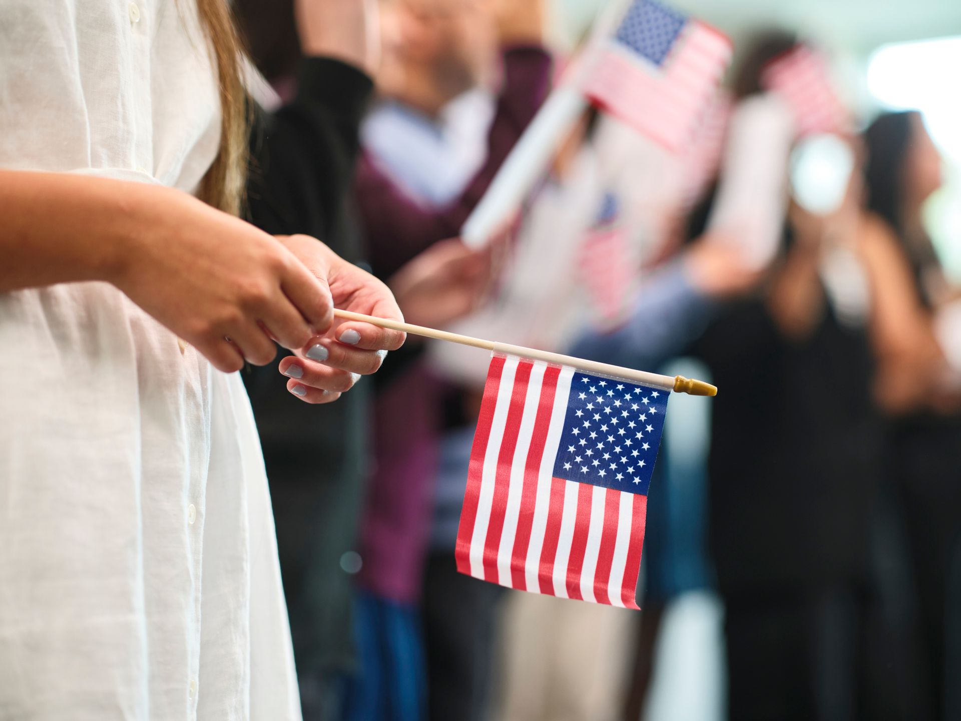 A woman is holding a small American flag in her hand.