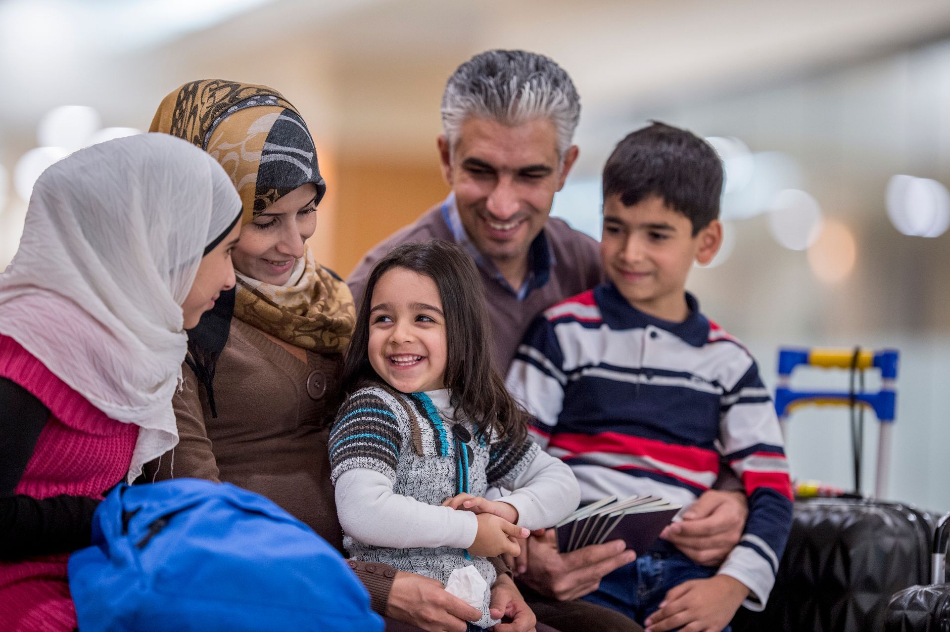 A group of people are sitting around a little girl at an airport.