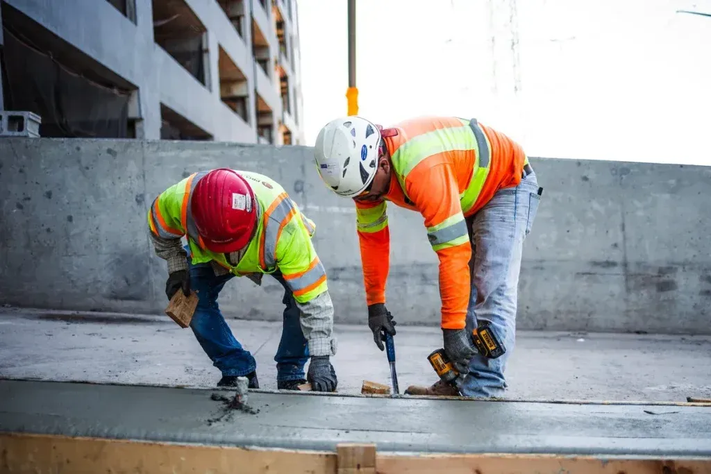 Two construction workers are working on a concrete surface.
