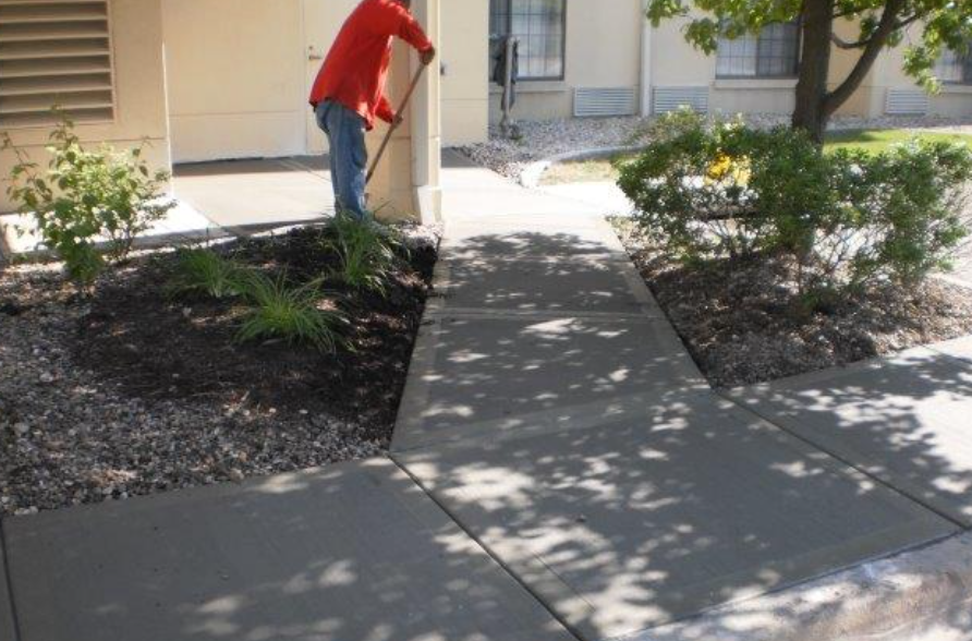 a man in a red jacket is raking a sidewalk