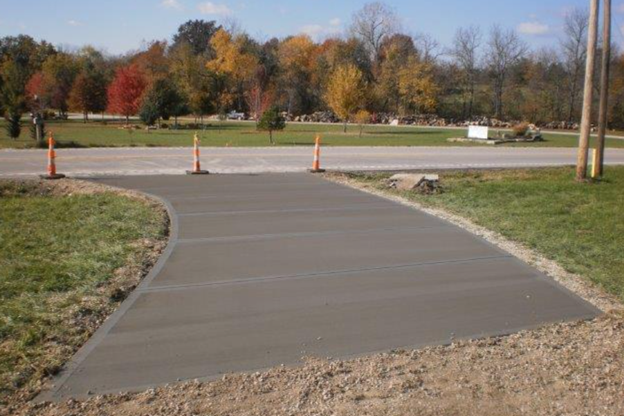 a concrete walkway leading to a park with trees in the background .